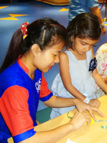 An instructor assists a young girl in making a beautiful rakhi during our craft workshop.