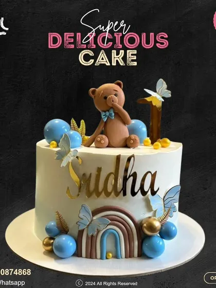 A whimsical first birthday cake featuring a cute teddy bear, a rainbow, and delicate blue butterflies. This personalized design is a sweet way to celebrate a special milestone.