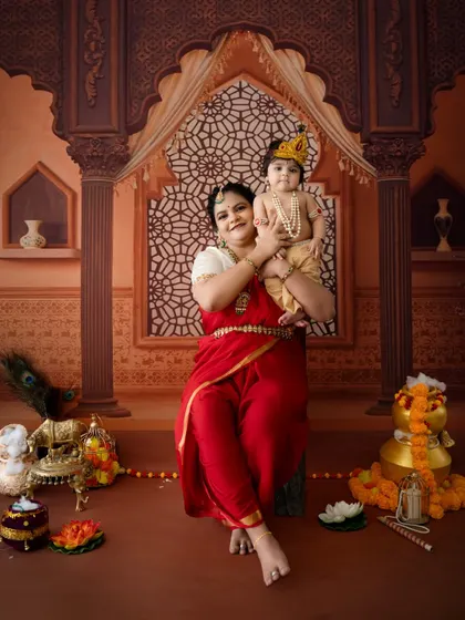 A stunning portrait of a mother holding her little Krishna in a grand, palace-themed setup.