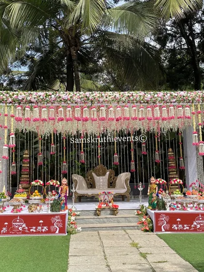 An expansive outdoor Seemantha decoration that is both grand and elegant. The stage is framed with pink and white flowers, with delicate floral strings creating a beautiful canopy effect.