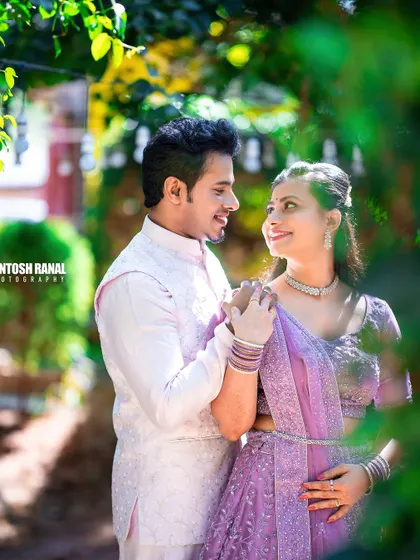 A soft and dreamy portrait of a couple in pastel traditional wear, framed by greenery.