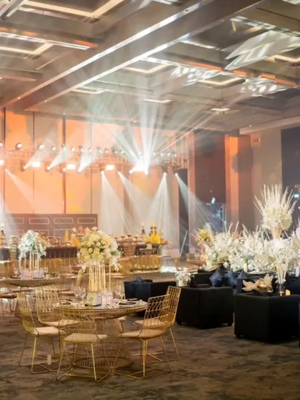 The Sangeet hall is filled with gold tables and chairs, with dramatic lighting creating a luxurious atmosphere.