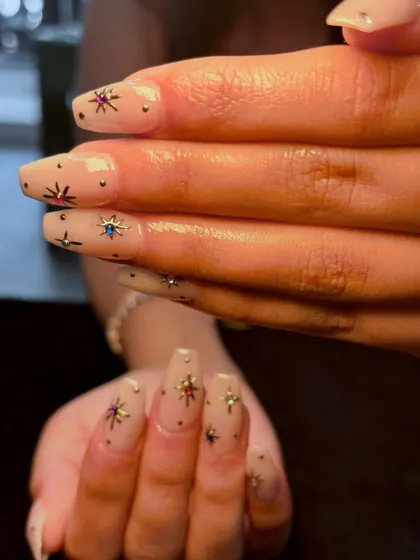 A different perspective of the starry nude manicure, showing how the gems and metallic stars are placed across the nails.