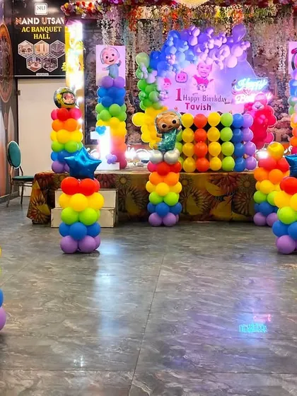 A Cocomelon themed first birthday setup in a hall, with rainbow balloon pillars topped with star foil balloons, creating a festive and symmetrical look.