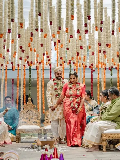 A beautiful wide shot of the wedding ceremony, showing the couple surrounded by their loved ones under a stunning floral mandap.