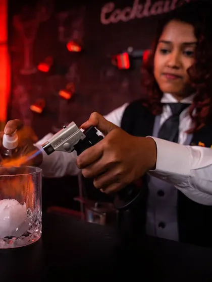 A bartender uses a torch to add a smoky aroma and visual flair to a cocktail. This technique is part of our molecular mixology offering, designed to create a multi-sensory experience.