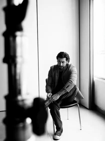 A black and white BTS shot from a men's portfolio session. The out-of-focus stand in the foreground frames the subject, adding depth and giving a true behind-the-lens perspective of the shoot.