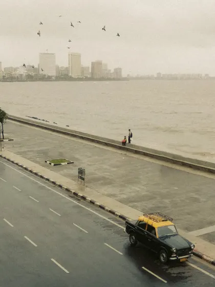 A kaali-peeli taxi parked by the sea wall at Marine Drive. The image evokes a sense of nostalgia and the countless journeys this iconic cab has made along the city's most famous promenade.