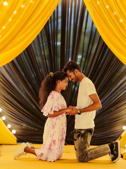 A romantic kneeling pose under a dramatically lit yellow curtain. The lighting creates a very theatrical and memorable pre-wedding photo.