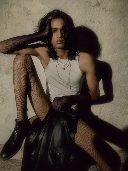 A seated pose that is both relaxed and intense. The styling and lighting create a moody, gothic-inspired fashion look.