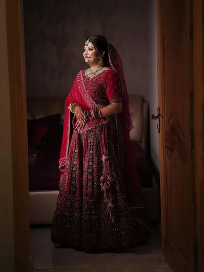 A classic bridal portrait taken through a doorway, capturing the bride in her beautiful red lehenga.