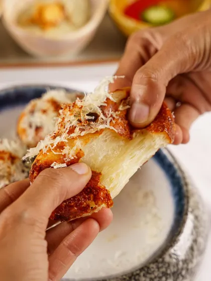 Hands pulling apart cheesy garlic bread. This action-oriented shot focuses on the satisfying cheese pull, a highly engaging visual for social media content.