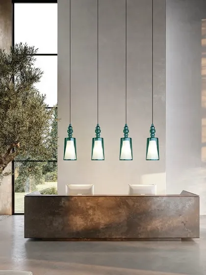 A row of four pendants in a striking green glass, installed over a reception desk. This demonstrates their suitability for commercial and hospitality applications, adding a touch of color and sophistication.