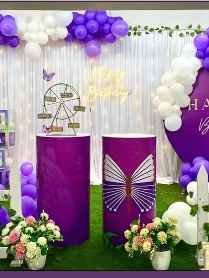 A royal purple butterfly theme with a white curtain backdrop. The decoration includes a Ferris wheel prop and large, colorful butterfly cutouts.