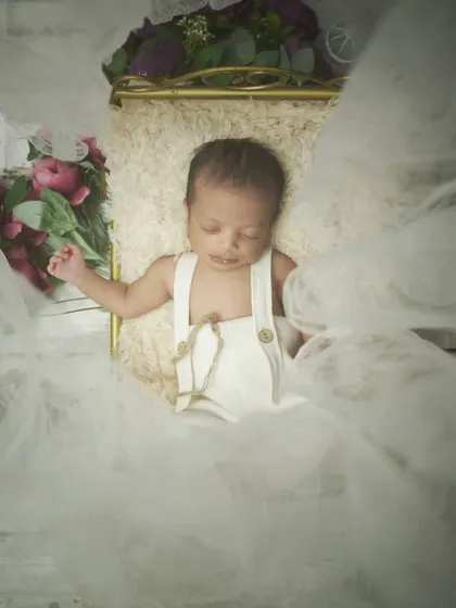 Another angle of the newborn in white overalls, surrounded by soft, white tulle. This creates an angelic and ethereal feel.