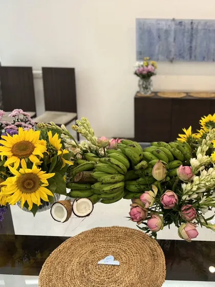 A stunning tablescape centerpiece for a traditional welcome, featuring a vibrant mix of sunflowers, pink lotuses, and green bananas, symbolizing abundance and auspicious beginnings.