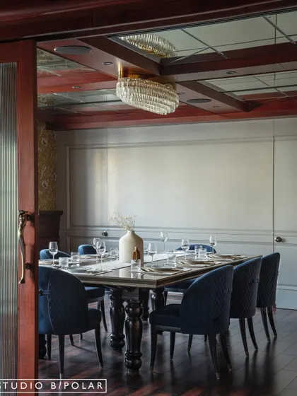 In contrast, the family dining area is designed for a cozier, more intimate feel. Deep blue chairs, rich wood tones, and a mirrored ceiling with a crystal chandelier create a warm and moody atmosphere.