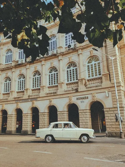 A vintage Fiat driving past the Hermes building at Horniman Circle, a perfect blend of classic car and classic architecture.