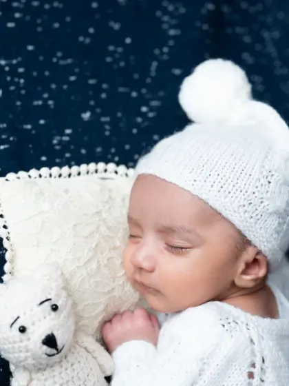 A close-up portrait of the sleeping baby boy in his white knit hat.