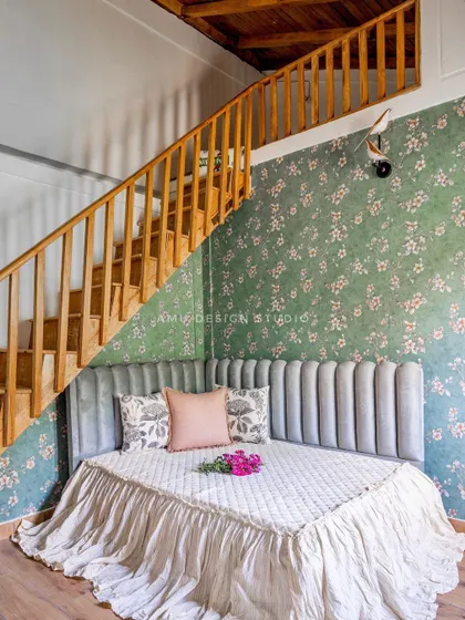 A cozy reading nook created under the stairs in a duplex bedroom. We designed a custom daybed with a fluted, grey velvet headboard, set against a charming green floral wallpaper.
