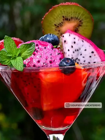 A vibrant fruit cocktail dessert served in a martini glass. It features jelly, fresh fruits like dragon fruit and kiwi, and a scoop of sorbet, making it a visually stunning dessert.