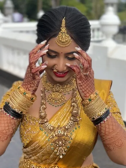 A happy bride in a golden yellow silk saree. The drape is styled to beautifully display the heavy embroidery and the stunning temple jewelry, creating a radiant bridal look.