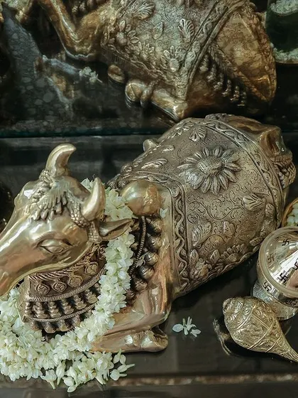 An overhead shot of a table decorated for a puja. The display includes brass idols, a conch shell (shankh), cinnamon sticks, and bowls of fresh jasmine, creating a feast for the senses.