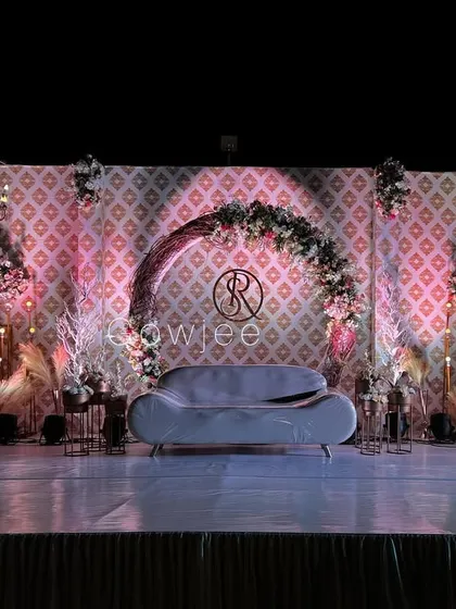 A modern reception stage with a patterned backdrop, a floral semi-arch, and a stylish grey sofa.