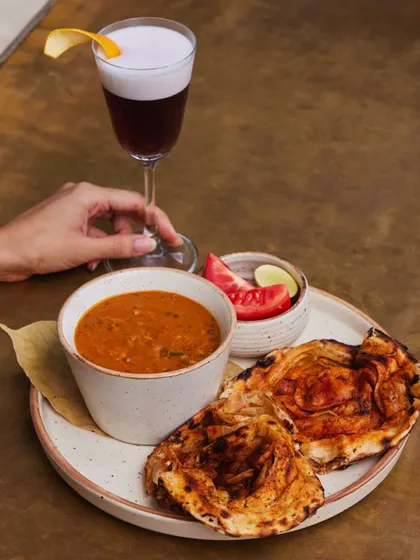 A perfect pairing. Our rich dal makhani with a flaky lachha paratha, accompanied by a deep, dark cocktail. Comfort food, elevated.
