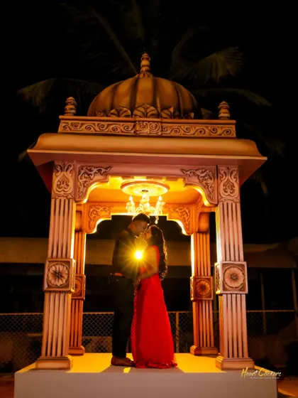 A couple shares a kiss under a beautifully lit gazebo at night. The warm light and intimate pose make this a classic romantic portrait.