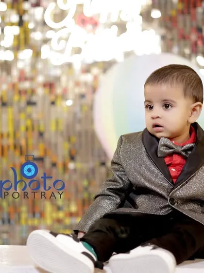 A handsome little boy in his formal suit and bow tie, sitting in front of a sparkling backdrop at his first birthday party.