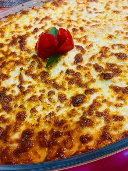 A large glass dish of my spinach and corn bake, with a beautifully browned cheesy crust and a small tomato rose garnish.