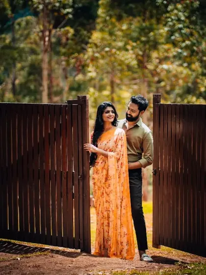 A couple shares a quiet moment by a wooden gate in a lush, green setting. A perfect example of a romantic and rustic pre-wedding photo.