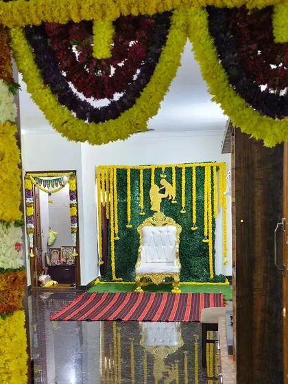 A complete baby shower setup viewed from the entrance of the room. The decoration includes a throne chair placed against a green backdrop with hanging yellow flower strings.