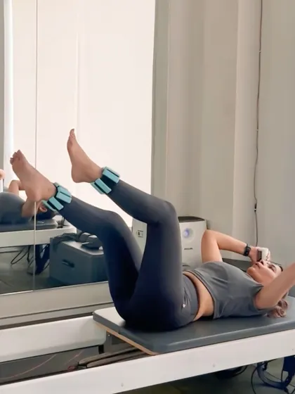 A client performs leg lifts with ankle weights on the reformer carriage. This exercise is excellent for targeting the lower abdominals and hip flexors with precision.
