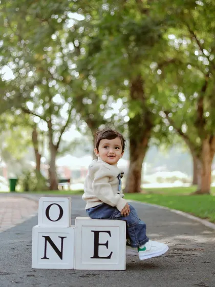 A happy one-year-old sitting proudly on top of his 'ONE' blocks during his outdoor birthday shoot.