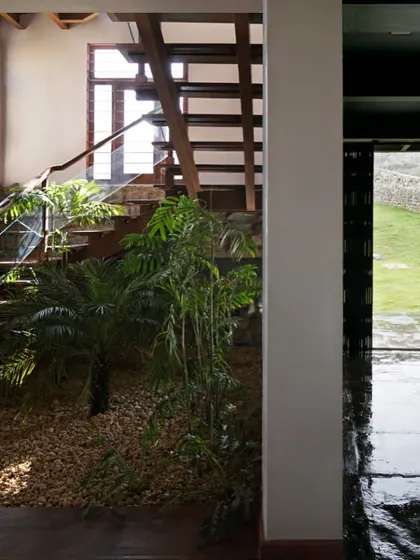 The floor at the base of the staircase is filled with local river gravel and indoor plants. This indoor landscaping, combined with the stone wall and timber stairs, creates a rich tapestry of natural textures.
