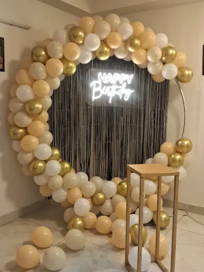 A full view of the chic birthday backdrop with a gold, cream, and white balloon garland. The circular frame and neon sign create a modern and stylish look.