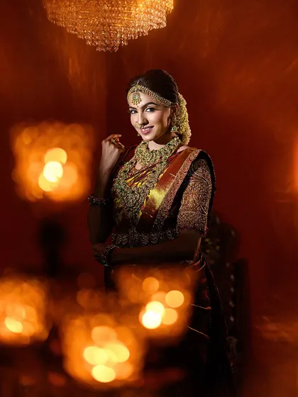 This portrait uses creative framing with foreground bokeh to draw the viewer's eye to the bride. The warm, ambient light creates a magical and celebratory feel.