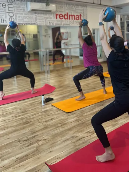 A group of women in a barre class, using Pilates balls to engage their core and upper body while performing squats.
