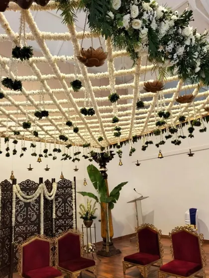 A closer look at the mandap stage, showing the carved wooden screen and the rich velvet chairs that await the couple, set against a backdrop of intricate floral work.