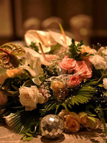 A centerpiece bouquet featuring soft roses and exotic anthuriums, with a mini disco ball nestled among the flowers. This playful detail adds a fun twist to the elegant arrangement.