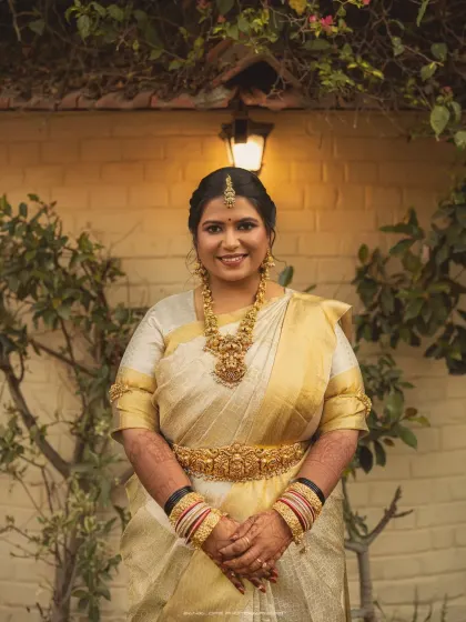 A portrait of the bride in a beautiful white and gold saree, her smile warm and welcoming. The soft lighting enhances her natural bridal glow.
