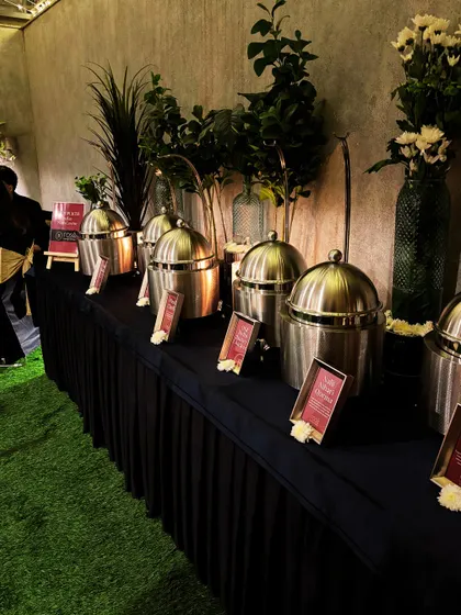 An elegant buffet setup on a green lawn, perfect for an outdoor corporate event. The combination of sleek, modern serveware and natural elements creates a sophisticated yet relaxed atmosphere.