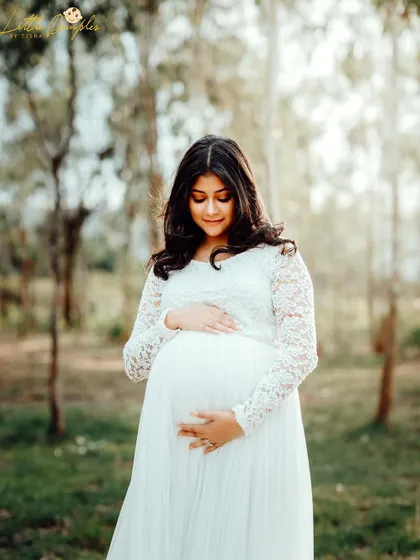 A stunning solo portrait of a mom-to-be in a white lace dress, surrounded by the peacefulness of the woods. She looks absolutely radiant.