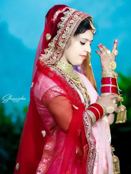 An elegant three-quarter portrait of the bride, her pose highlighting the flow of her red dupatta and her wedding bangles.