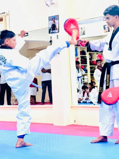 A student practices a high kick on a target held by a senior. This drill helps improve accuracy, height, and power.