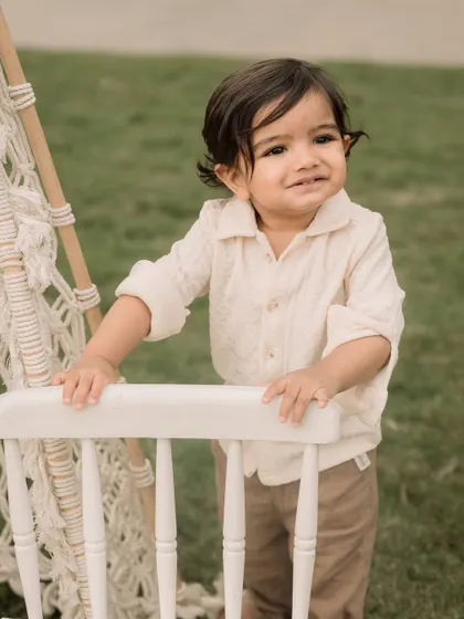 A toddler stands proudly by a chair, taking a break from his outdoor explorations.