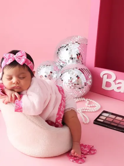 A little diva in dreamland. This Barbie-themed newborn shoot is full of fun and glamour. Here, our little model is styled with a tiny robe and accessories for a playful and fashionable portrait.