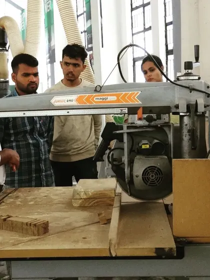 Students gather around a radial arm saw for a demonstration. We emphasize understanding the mechanics and safe use of every machine in our workshop.